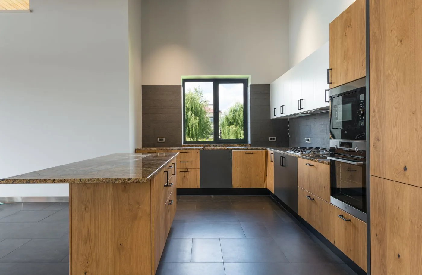 Cuisine avec façades de chêne, îlot et plan de travail en pierre sombre. Référence d’association de matières.