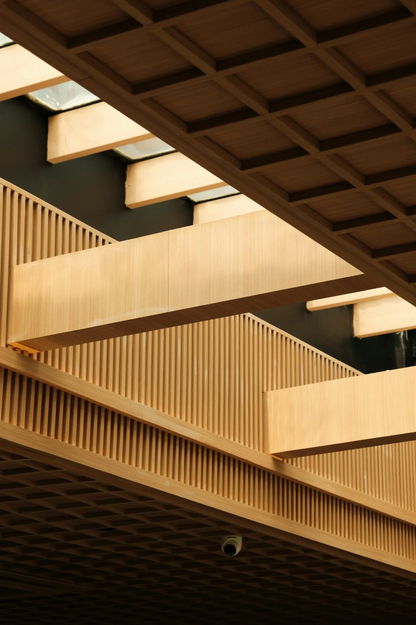 Poutres et garde-corps en bois clair, traversés par une lumière chaude. Photographie d’inspiration architecturale.