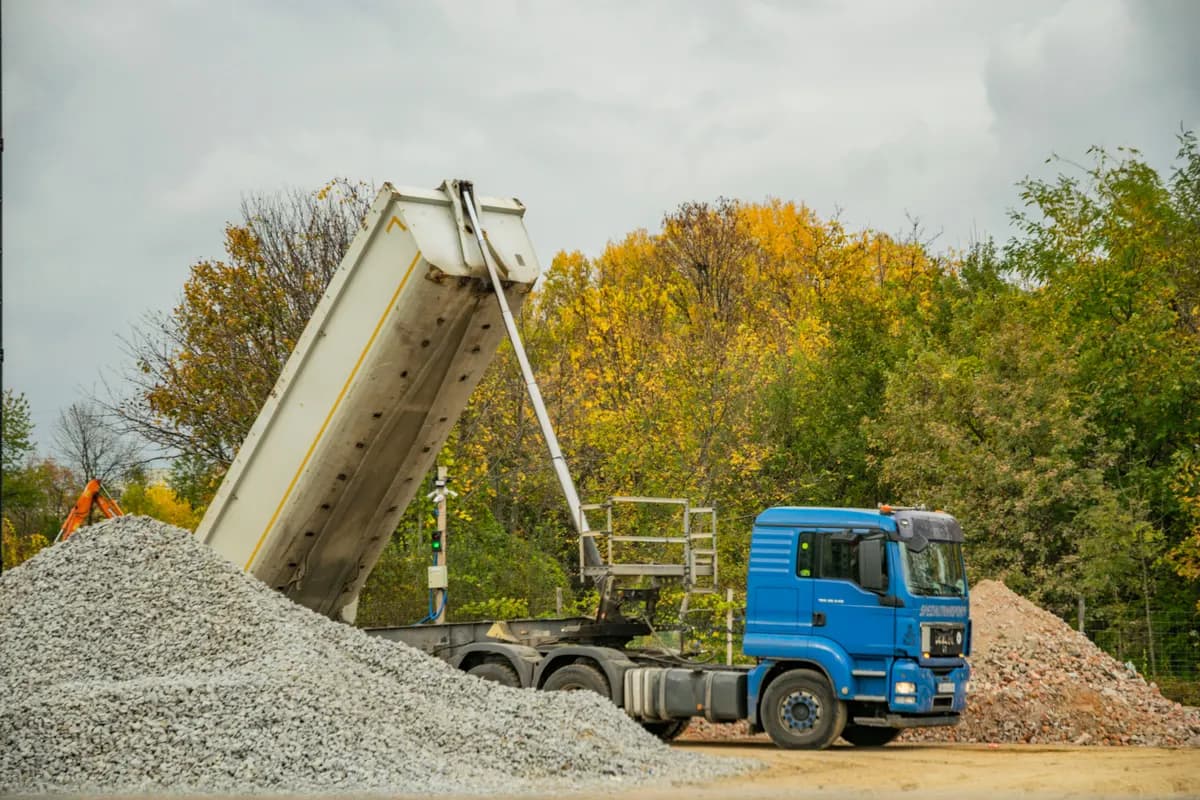 Un camion-benne décharge un tas de granulats gris sur un chantier.