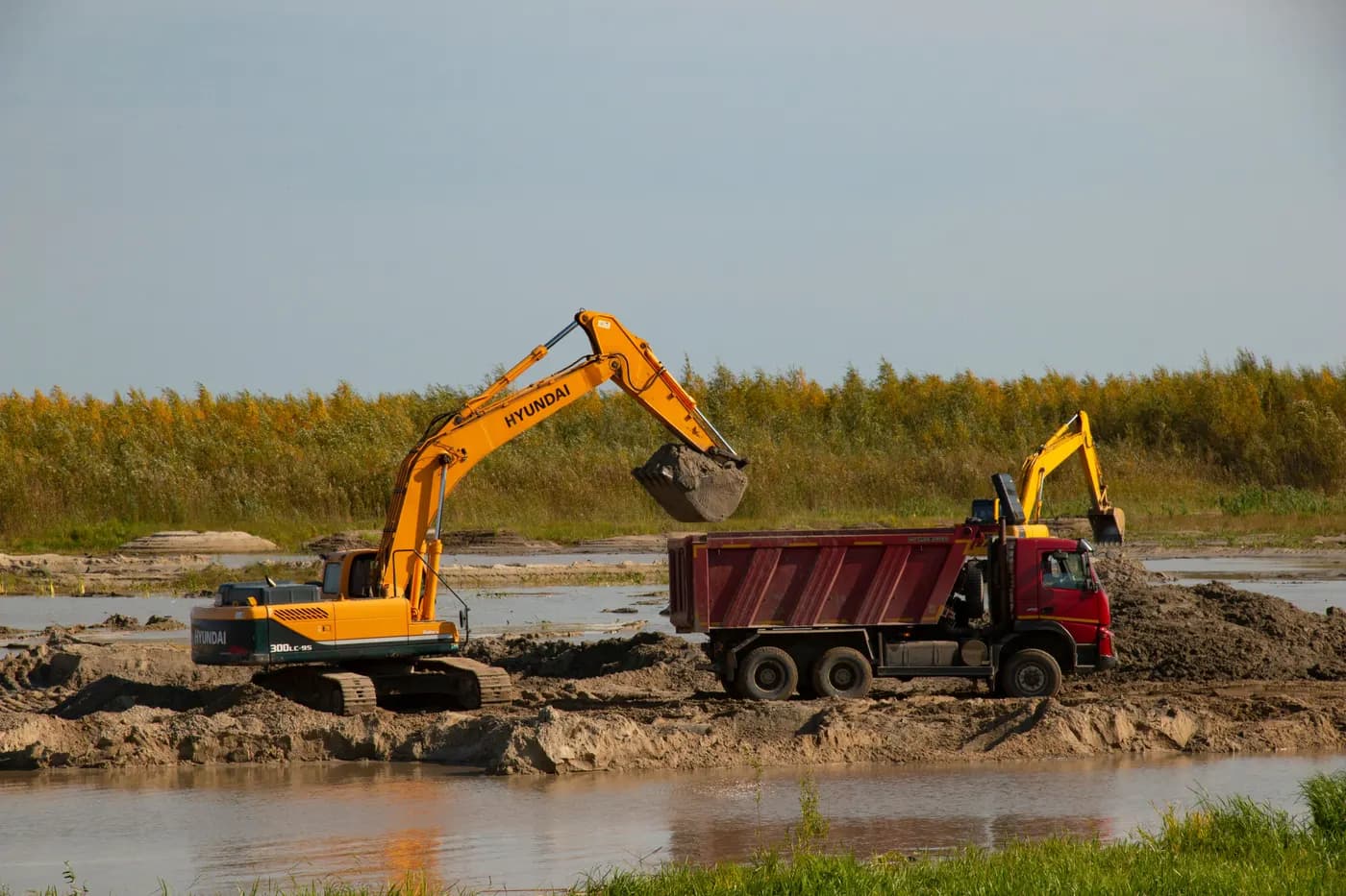 Une pelle charge un camion-benne de terre au bord d’une excavation humide.