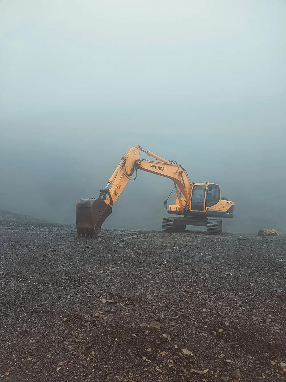 Une pelle mécanique immobile sur un terrain dénudé dans une brume épaisse.