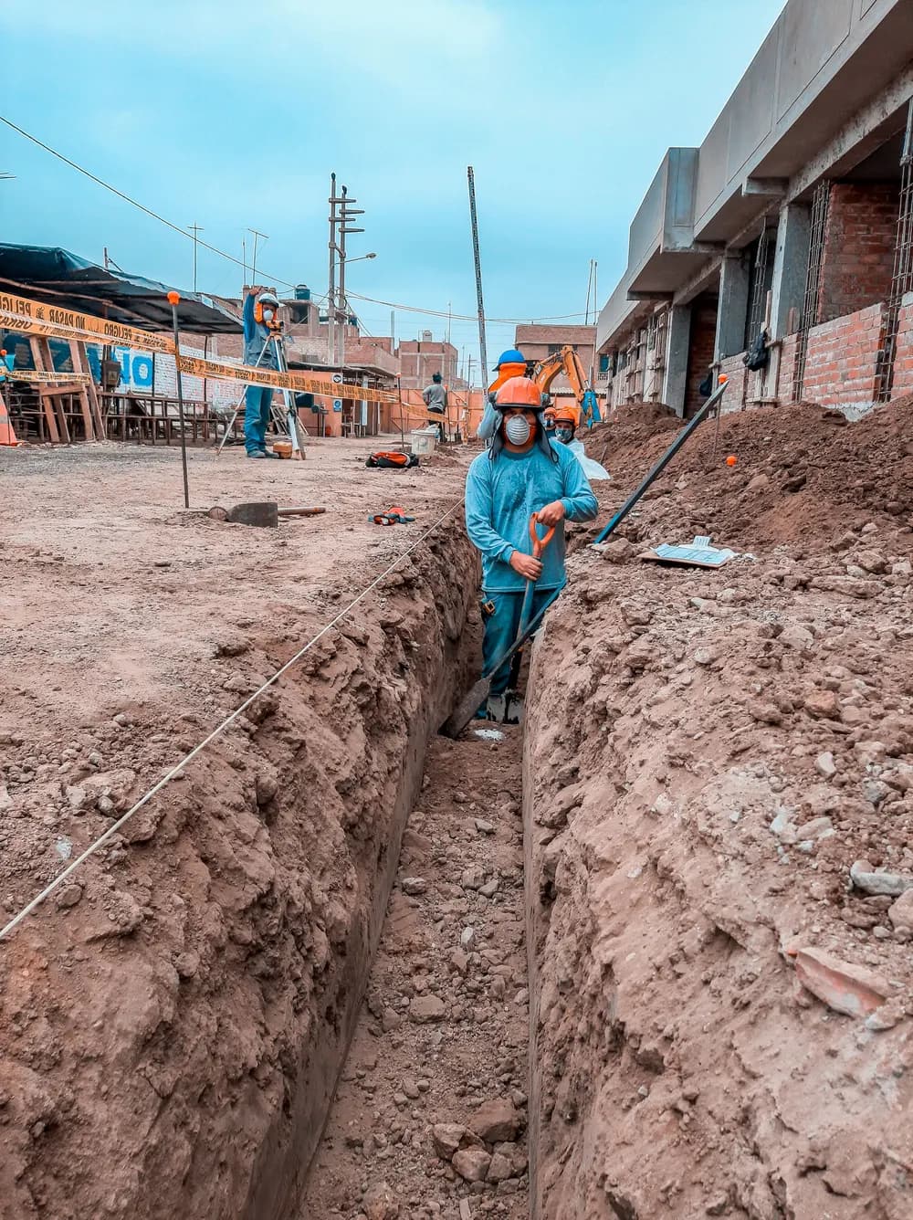 Des ouvriers équipés de casques travaillent dans une tranchée sur un chantier de construction.