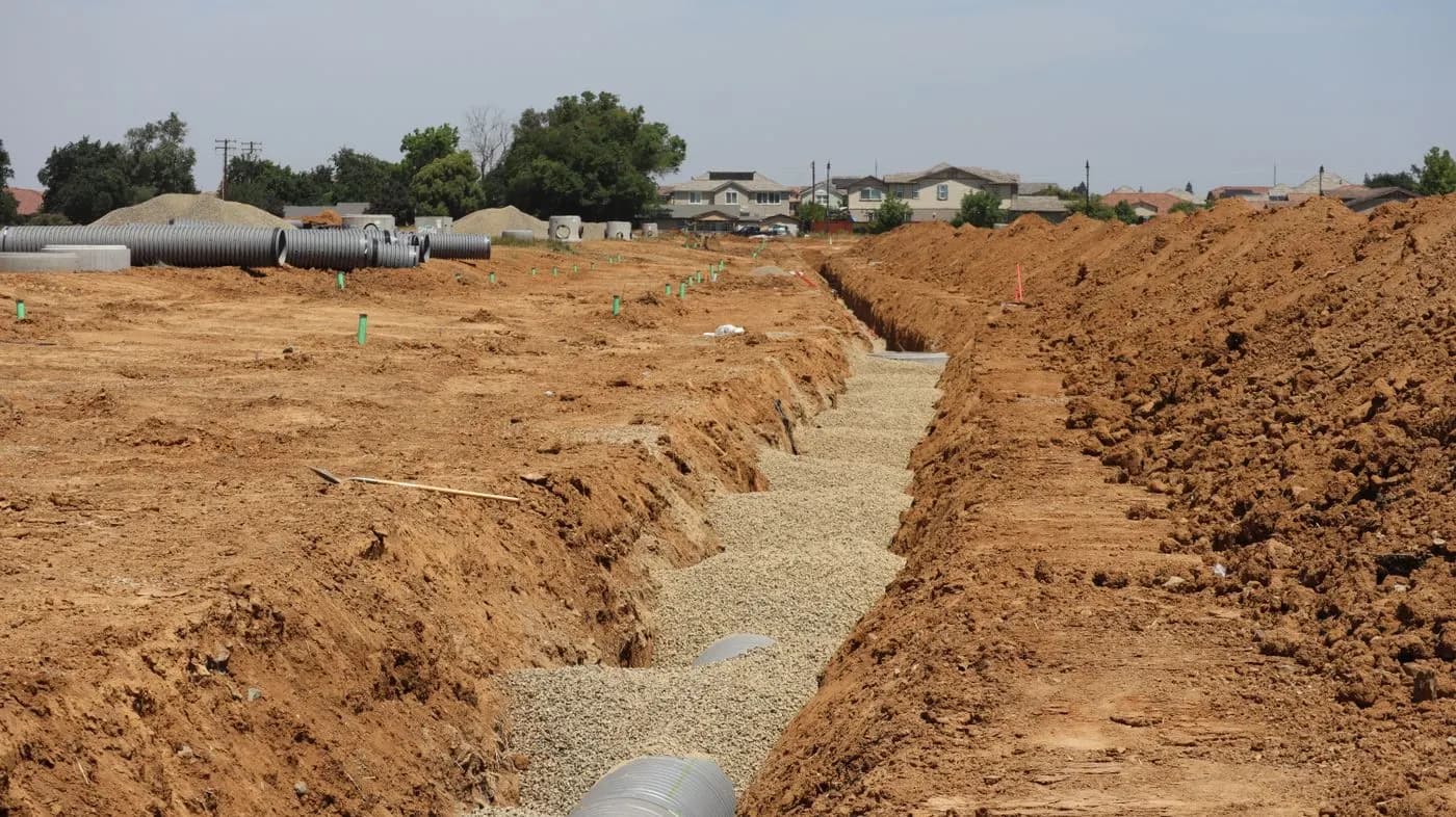 Tranchées ouvertes dans un terrain de construction, avec des conduites en attente de pose.
